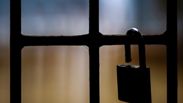 Prison bars close up, with a large padlock unopened